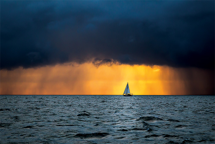 White sailboat in the open waters during sunset with a large storm approaching