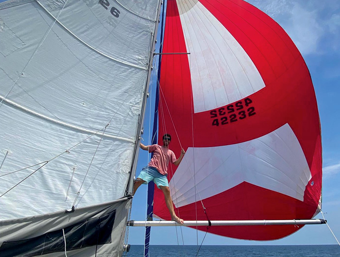 Young adult male standing on red and white sails while out on at sea