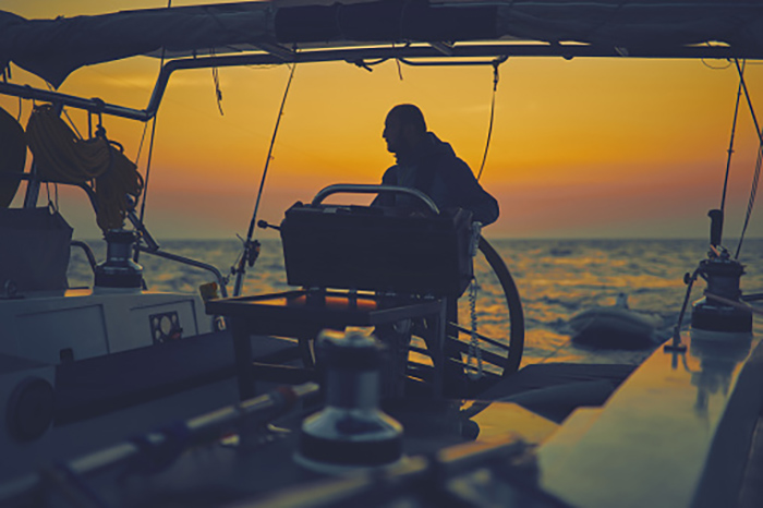 Man at the wheel of his vessel at sunset out at sea