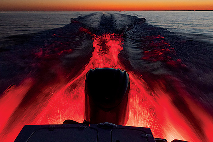 Back of a boat showing the motor lit by the red rear lights against the backdrop of a beautiful sunset