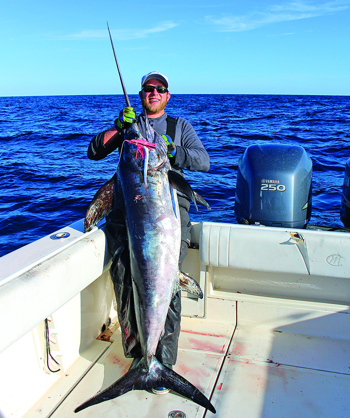 Adult male in the open waters on a white boat holding a large sword fish.