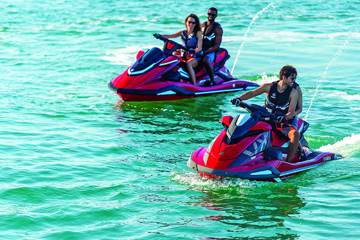 Young adults riding red jet ski's on a sunny day out on the water.