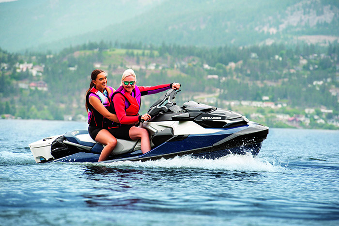 A senior woman and young adult female riding a blue and gray jet ski on the open water.
