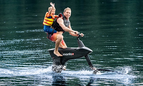 Adult male wearing a black life jacket cycling on the water with a young boy on his back.