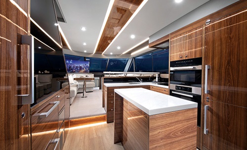 Inside cabin of a vessel featuring glossy wood cabinets, oven, island and track lighting.
