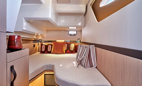 Interior cabin of a boat featuring a white couch and seating area, track lighting and brown wood paneling and cabinets.