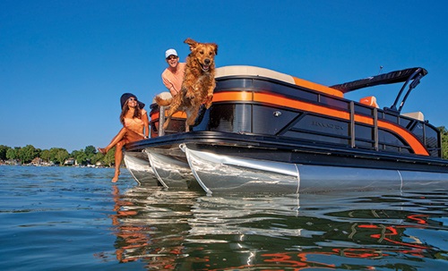 Adult female and adult male aboard a black and orange pontoon boat watching a dog leap into open waters.