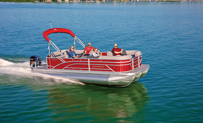 Four middle-aged adults aboard a silver and red pontoon boat cruising a lake.