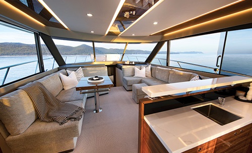 Interior cabin of a vessel featuring oval tan seating area, track lighting and windows.
