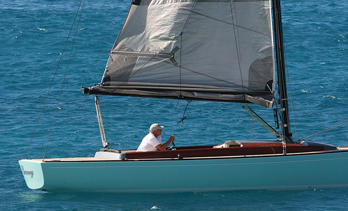 An adult male on a sailboat in open blue waters on a sunny day.