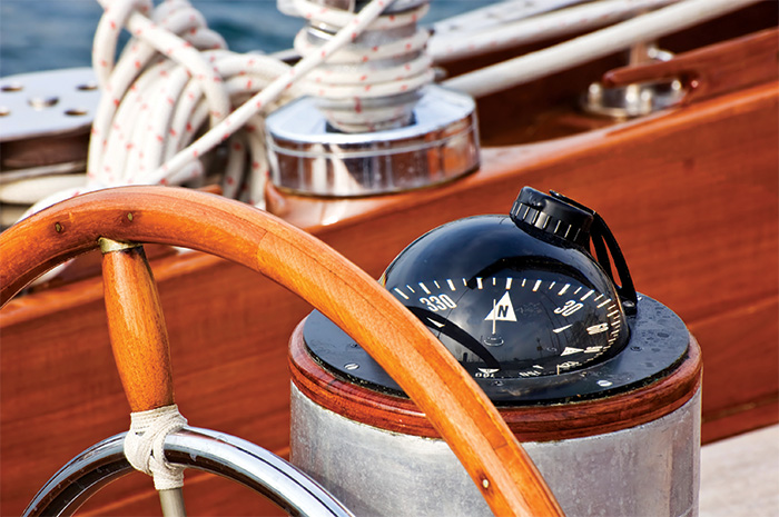 Close-up image of a vessel steering wheel with a dark varnish and large compass.