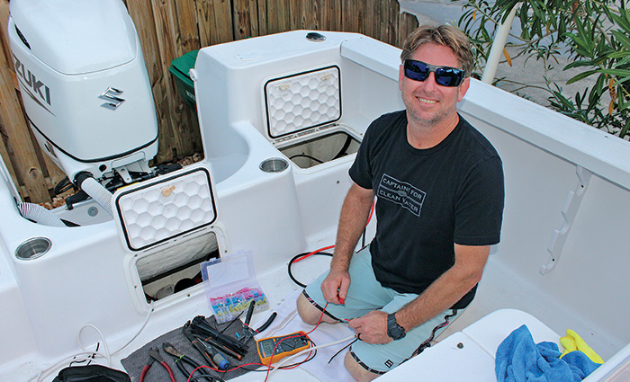 Middle-aged man wearing a navy shirt, light blue shorts and sunglasses restoring his boat.