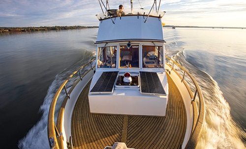 Panoramic view from the front of a white vessel facing the back while speeding on open waters at sunset.