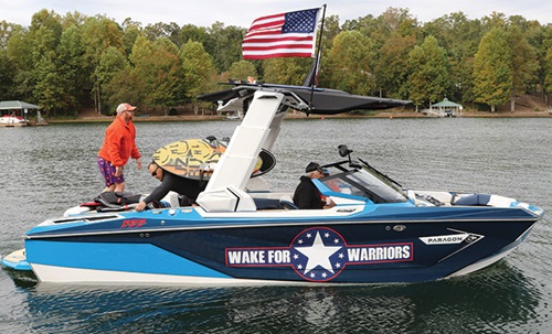 Adults aboard a blue and white speed boat with a large American flag and 'Wake For Warriors' decal on the side.