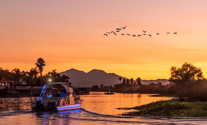 A glowing pontoon boat at sunset with Mount Diablo in the background.